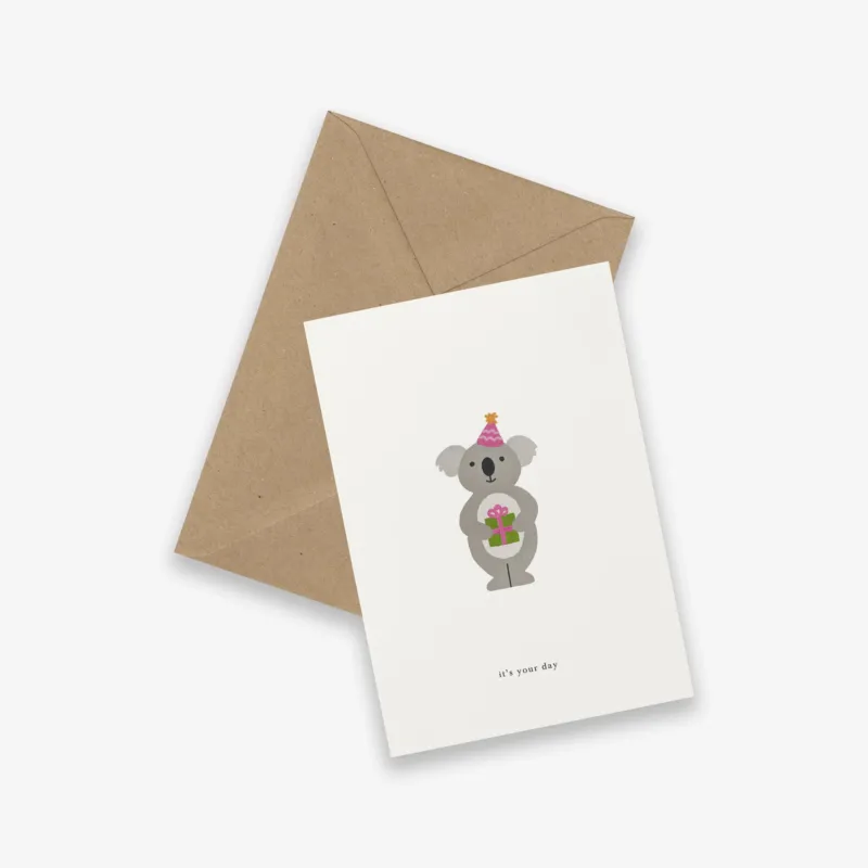 Greeting card with a koala illustration and brown envelope on a white background. Birthday card with the text 'it's your day'