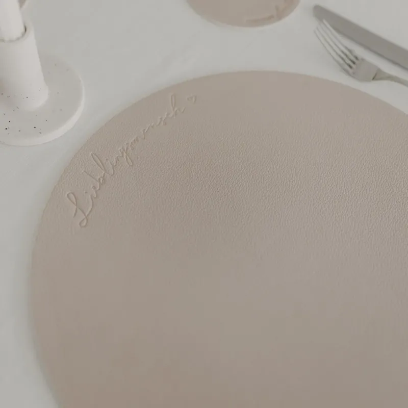 Rundes cremefarbenes Platzset mit Prägung „Lieblingsmensch“ auf gedecktem Tisch.