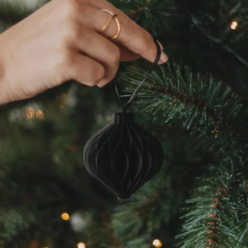 Schwarzer Papieranhänger in Kugelform wird als Christbaumschmuck am Weihnachtsbaum aufgehängt