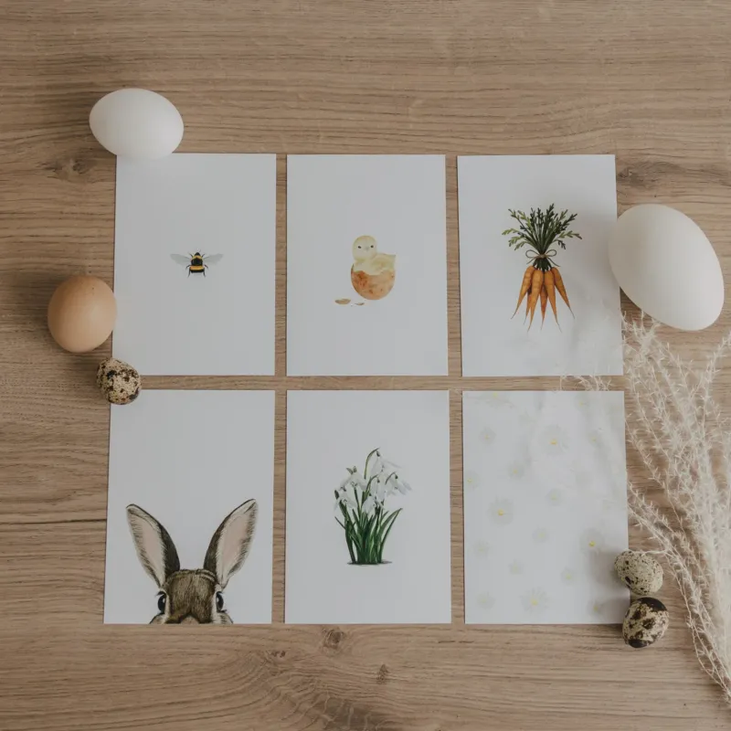 Sechs Aquarellkarten mit Oster-Motiven auf Holztisch, dekoriert mit Eiern.