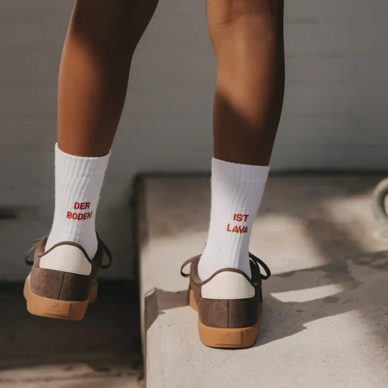 Kind in weißen Socken Der Boden ist Lava mit rotem Schriftzug beim Balancieren auf einer Kante.
